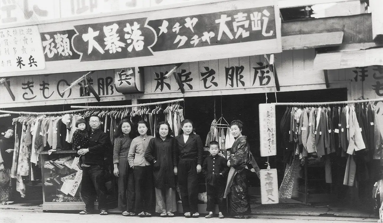 Historical black-and-white photograph of KOMEHYO's original clothing store in Nagoya around 1947, with staff standing in front of displayed garments.