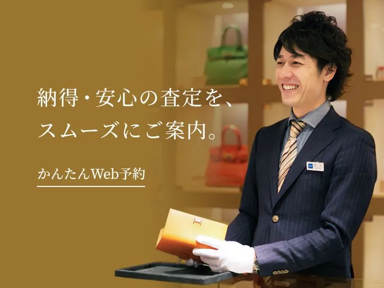 「納得・安心の査定を、スムーズにご案内。かんたんWeb予約」というテキストと、高級ブランドバッグが並ぶ店内で笑顔で接客する男性スタッフの画像。